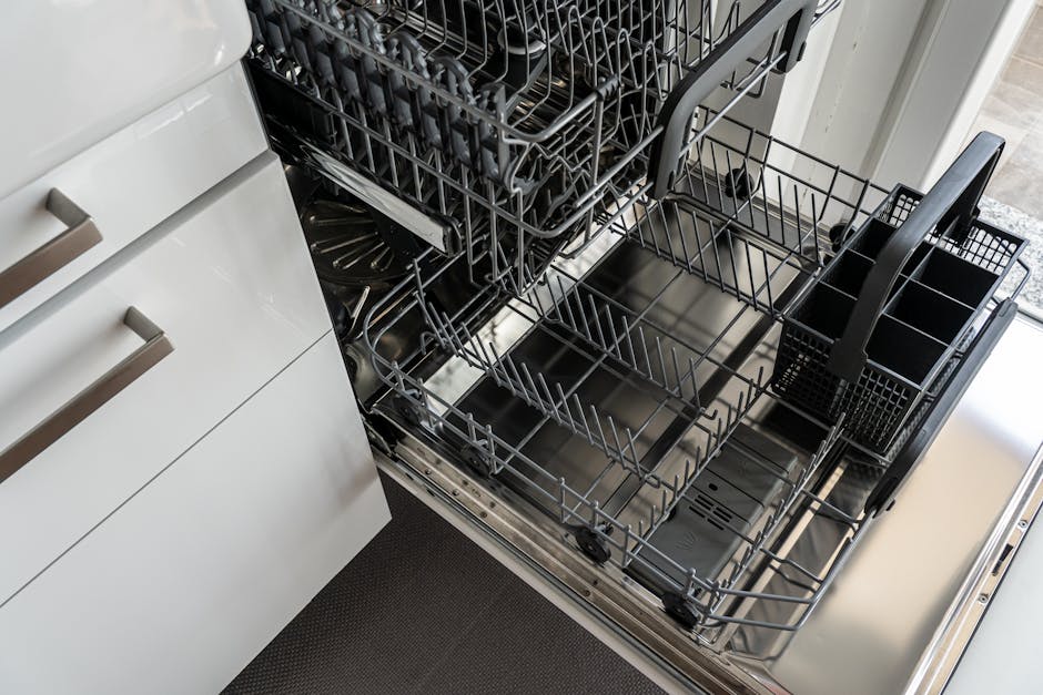 A clean and empty stainless steel dishwasher open in a modern kitchen setting.