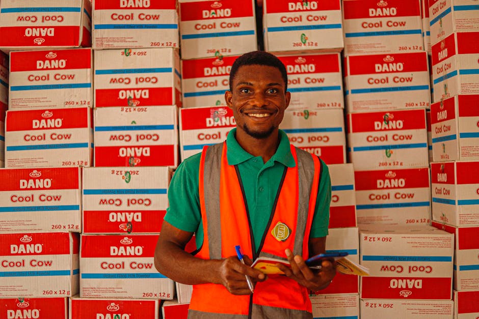 Portrait of a cheerful warehouse worker in front of Dano Cool Cow boxes, showcasing inventory management.
