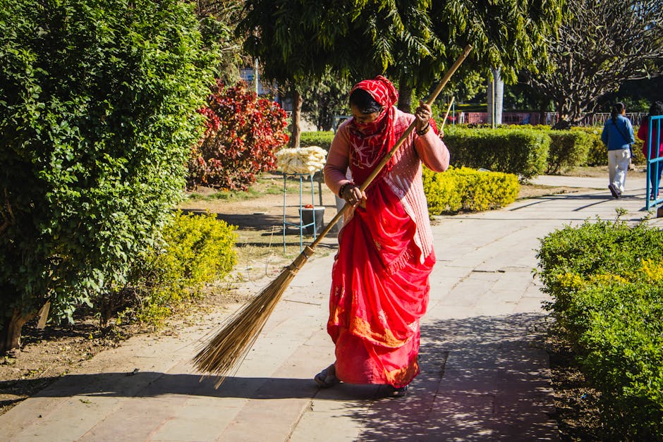 Μια γυναίκα που σκουπίζει ένα μονοπάτι κήπου κάτω από το φως του ήλιου.